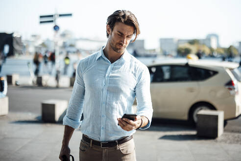 Geschäftsmann Textnachrichten über Smartphone an einem sonnigen Tag - GUSF07155