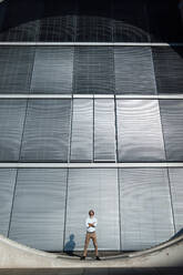 Geschäftsmann steht mit verschränkten Armen vor einem modernen Gebäude an einem sonnigen Tag - GUSF07187