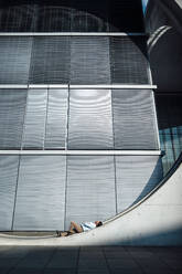 Businessman lying on wall in front of modern building - GUSF07188