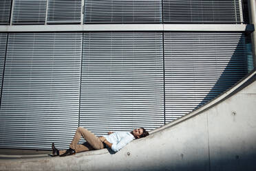 Businessman lying on wall in front of modern building - GUSF07190