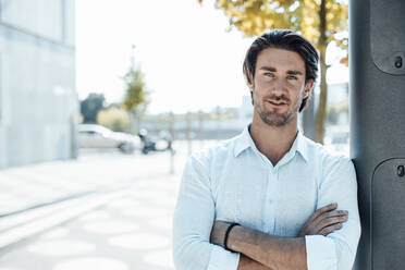 Smiling handsome businessman standing with arms crossed in city - GUSF07195