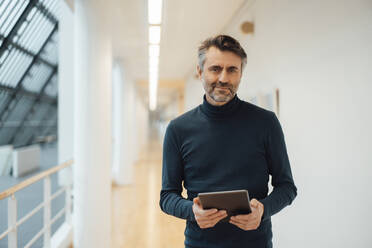 Businessman with tablet PC in corridor at office - JOSEF07404