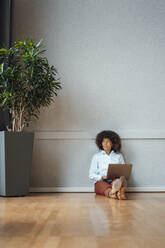 Geschäftsfrau mit Laptop, die vor einer Wand im Büro nachdenkt - JOSEF07441