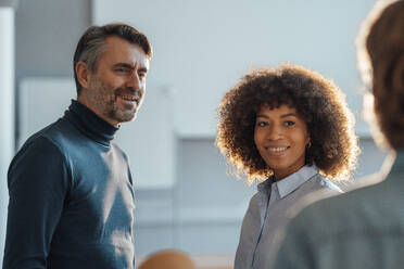 Smiling multiracial colleagues looking at businessman in office - JOSEF07445