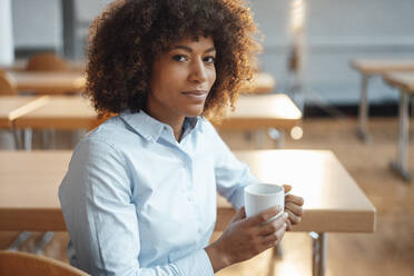 Lächelnde Geschäftsfrau mit Kaffeetasse am Arbeitsplatz sitzend - JOSEF07468