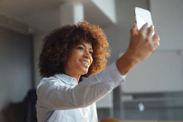 Glückliche Geschäftsfrau nimmt Selfie durch Handy im Büro - JOSEF07471