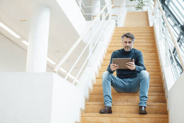 Businessman with tablet PC sitting on steps in office - JOSEF07473