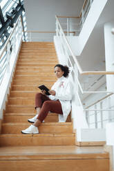 Healthcare worker with tablet PC sitting on staircase in medical clinic - JOSEF07517