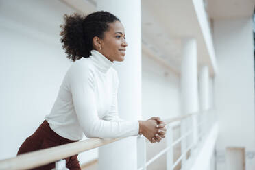 Smiling working woman day dreaming in corridor at office - JOSEF07525