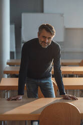 Smiling working man leaning on desk at work place - JOSEF07569