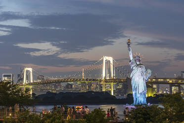 Japan, Region Kanto, Tokio, Nachbildung der Freiheitsstatue und beleuchtete Regenbogenbrücke in der Abenddämmerung - FOF12965