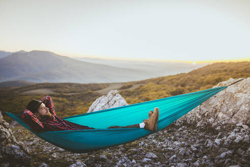 Man lying on hammock in mountain range - TETF00756