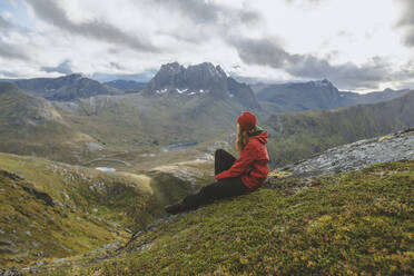 Junge Frau in roter Jacke auf einem Berg sitzend - TETF00765