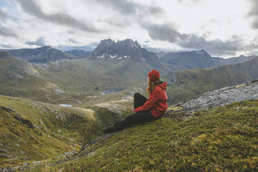 Young woman in red jacket sitting on mountain - TETF00765