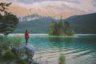 Germany, Bavaria, Eibsee, Young woman standing on rock by Eibsee lake in Bavarian Alps - TETF00770