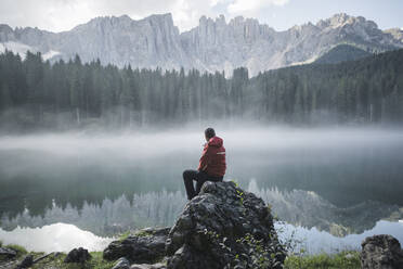 Schweiz, Junger Mann sitzt am Karersee in den Dolomiten in der Morgendämmerung - TETF00778