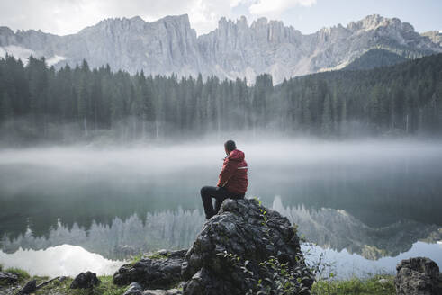 Schweiz, Junger Mann sitzt am Karersee in den Dolomiten in der Morgendämmerung - TETF00778