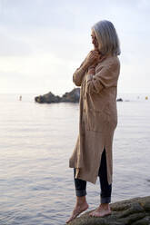 Frau mit geschlossenen Augen auf einem Felsen am Strand stehend - VEGF05380