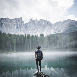 Italien, Carezza, Junger Mann steht auf einem Felsen am Lago di Carezza in den Dolomiten in der Morgendämmerung - TETF00839