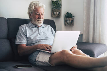 Senior man using laptop on sofa - TETF00880