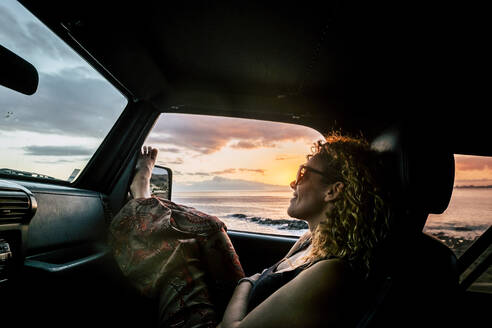 Frau im Auto mit angezogenen Beinen bei Sonnenuntergang - TETF00882