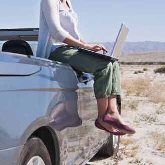 USA, Kalifornien, Palm Springs, Frau sitzt auf der Seite eines Cabriolets in der Wüste und benutzt einen Laptop - TETF00909
