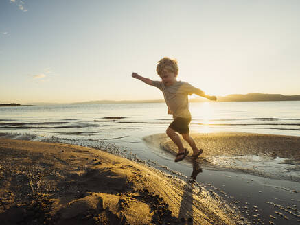 Kleiner Junge (4-5), der an einem sonnigen Tag über Wasser springt - TETF01018