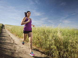 Mid adult woman jogging on path through field - TETF01029