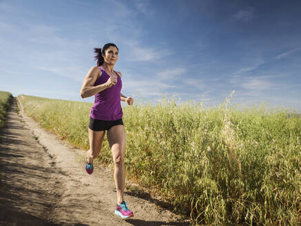 Mittlere erwachsene Frau joggt auf einem Weg durch ein Feld - TETF01029
