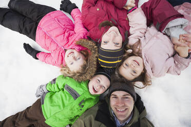 Unmittelbar darüber Porträt von drei Kindern (2-3, 4-5) mit Eltern im Schnee liegend - TETF01038