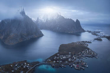 Stadt mit Wohnhäusern auf der grasbewachsenen Insel Lofoten in der Nähe des ruhigen Meeres vor einer rauen Felswand und einem düsteren Himmel in Norwegen - ADSF33813