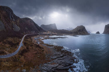 Meer mit schäumenden Wellen umgeben von hohen felsigen Klippen mit Straße gegen grauen bedeckten Himmel in der Natur von Norwegen gelegen - ADSF33815