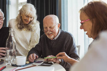 Lächelnde ältere Freunde benutzen ihr Smartphone am Tisch im Pflegeheim - MASF28958
