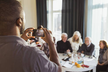 Männlicher Pfleger fotografiert ältere Männer und Frauen mit dem Smartphone im Pflegeheim - MASF28960