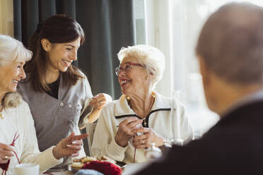 Lächelnde Krankenschwester im Gespräch mit strickenden Seniorinnen im Pflegeheim - MASF28976