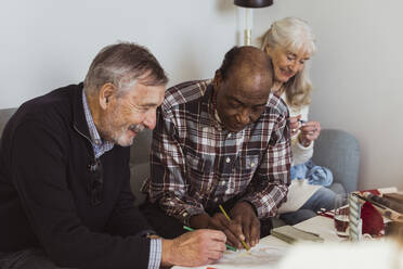 Lächelnde ältere Männer, die von einer Freundin im Pflegeheim auf Papier gezeichnet werden - MASF28980