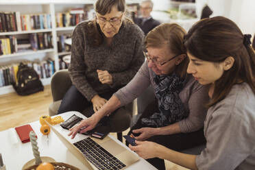 Elderly woman learning online shopping on laptop from female healthcare worker in nursing home - MASF28985