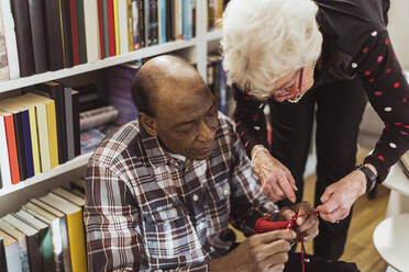 Elderly man knitting while female friend assisting him at retirement home - MASF28989