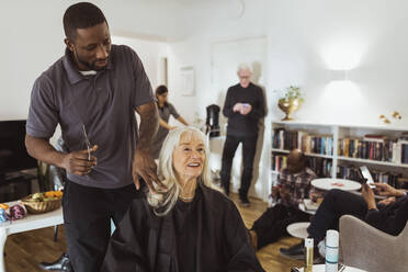 Male caregiver talking with senior woman while cutting hair in nursing home - MASF28990