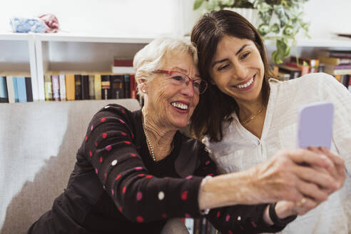 Smiling senior woman taking selfie with female caregiver in nursing home - MASF28993