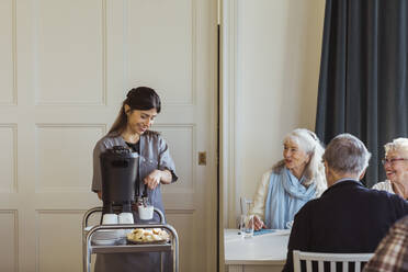 Lächelnde Mitarbeiterin im Gesundheitswesen serviert Kaffee an ältere Frauen und Männer im Altersheim - MASF29015