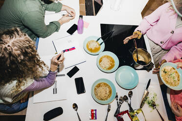 High angle view of multiracial young friends having noodles while studying at dining table in college dorm - MASF29063