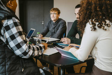 Lächelnde multirassische erwachsene Studenten, die gemeinsam an einem Tisch in der Cafeteria lernen - MASF29069