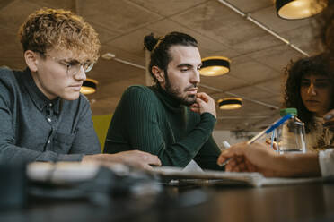 Young multiracial students sitting at table while studying together in cafeteria - MASF29071