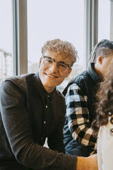 Porträt eines lächelnden blonden Mannes mit Brille, der in der Cafeteria einer Universität sitzt - MASF29078