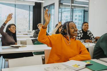 Weibliche Schüler heben die Hände, während sie im Klassenzimmer sitzen - MASF29095