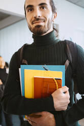 Smiling young man holding books in university - MASF29150