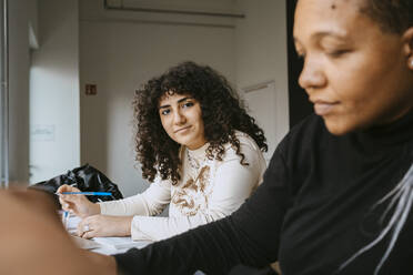 Portrait of woman with curly hair sitting by female friend in university - MASF29163