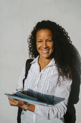 Portrait of smiling woman with curly hair holding book at college campus - MASF29202