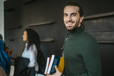 Porträt eines lächelnden Mannes mit Büchern in einer Volkshochschule - MASF29208